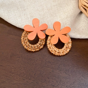 Detail of vintage rattan hoop earrings with orange floral resin on wood background