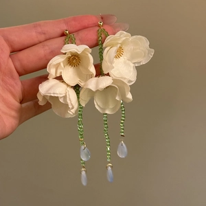 Dettaglio di orecchini a fiore in tessuto bianco con perline verdi e gocce blu pendenti