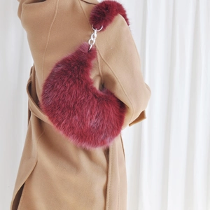 Detail of burgundy plush crescent bag with silver chain worn over a camel wool coat