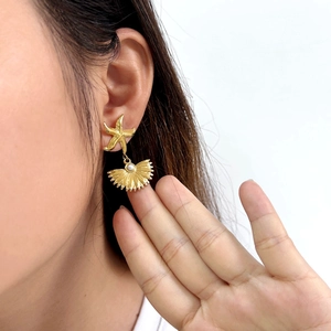 Detail of a gold starfish earring with a shell pendant and a white pearl on a model