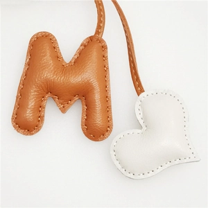Brown leather letter M bag charm with white heart pendant and stitched details