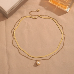 Double-layered gold titanium steel necklace with irregular pearl pendant on beige surface