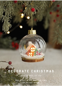 Detalle de bola de Navidad LED con casa en miniatura y muñeco de nieve en rama de pino