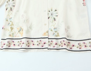 Makro-Detail des Leinenhemd-Saums mit elegantem Blumenmuster und Knopfverschluss vorne