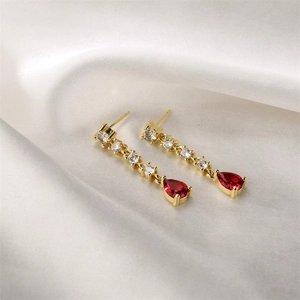 Détail de boucles d'oreilles dorées avec pierres goutte rouges et zircons blancs