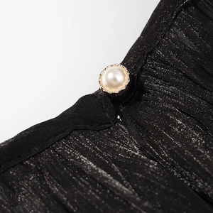 Détail macro d'une robe en tissu plissé noir avec un élégant bouton en perle