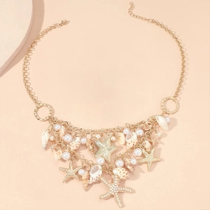 Close-up of golden starfish and seashell charms with white pearls on a layered necklace