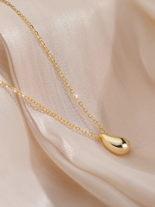 Detailed view of glossy gold teardrop pendant on elegant silk fabric background