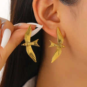 Macro view of gold flying bird earrings with detailed feather texture on model