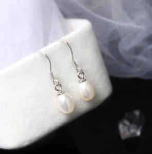 Macro detail of teardrop pearl earrings hanging on a white velvet jewelry box with lace