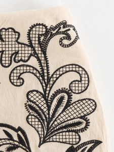 Detailed embroidery on beige fabric featuring intricate black patterns and openwork texture
