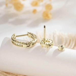 Luxury gold-plated zircon huggie hoop and stud earrings set on a white display pedestal
