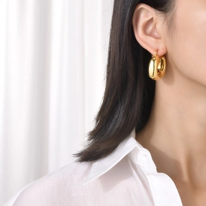 Polished 18K gold chunky hollow hoop earrings worn by a model in a minimalist style