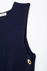 Detail of navy knit vest showing golden side buttons and fine fabric texture