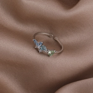 Close-up of pearl and zircon flower ring with blue and green gems on brown silk