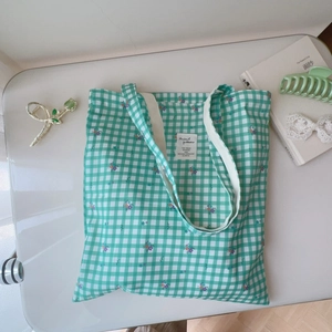 Flat lay of green gingham floral canvas tote bag with book and hair accessories