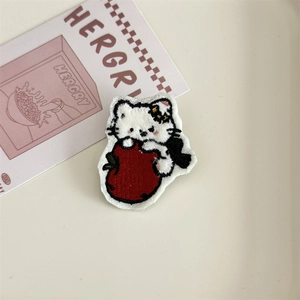 Close-up of embroidered white cat holding a red apple patch for clothing decoration