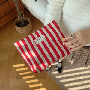 Model holding a red and white striped fabric toiletry bag in a natural home setting