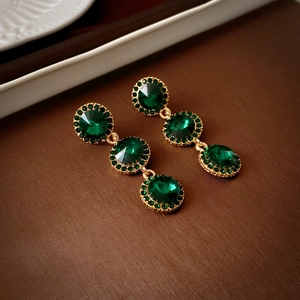 Gros plan de boucles d'oreilles pendantes vintage dorées et vert émeraude avec cristaux