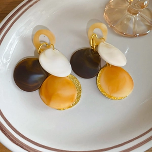 Macro view of geometric acrylic tassel earrings with amber resin discs on a ceramic plate
