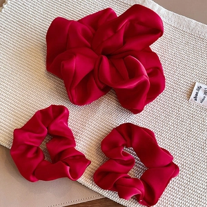 Elegant red satin scrunchies set with glossy finish on textured beige background