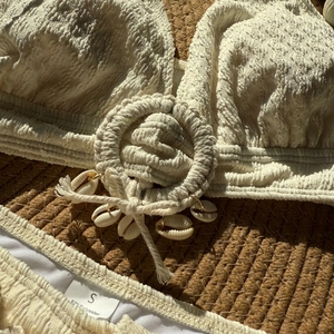 Detail of white textured bikini with woven ring and natural shell decor on straw background