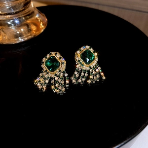 Macro detail of vintage gold earrings with square green gemstone and sparkling tassels
