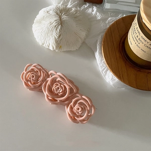 Detailed view of pink triple rose hair claw clip on a white desk with aesthetic props