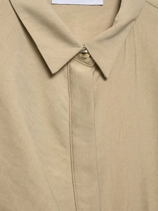 Detailed close-up of beige shirt neckline with elegant round golden metal button