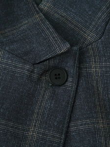 Close-up of a black four-hole button on dark grey plaid wool texture suit fabric