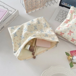 Detalle del neceser de lona crema con lazo azul y estampado floral en escritorio