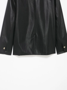 Detail of black coated leather jacket showing refined texture and buttoned cuffs