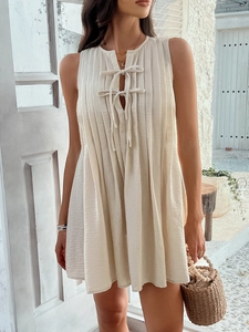 Detail of ivory sleeveless pleated dress featuring lace-up front and linen texture