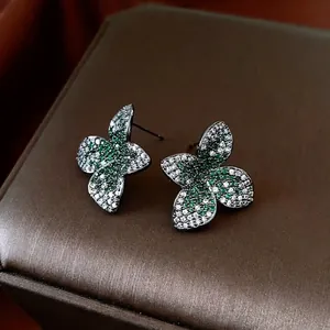 Vintage silver needle flower studs with green and white zircons on a textured jewelry box