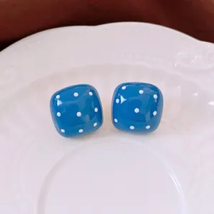 Chic blue dice-shaped earrings with white polka dots on a luxury ceramic plate