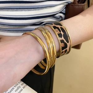 Close-up of a four-piece gold bracelet set with leopard print details on a model wrist