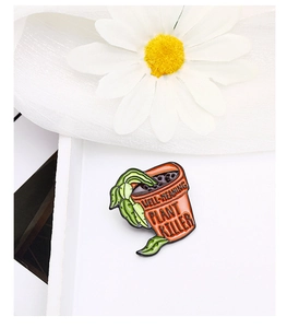 Détail du badge en émail avec pot orange et texte humoristique sur les plantes
