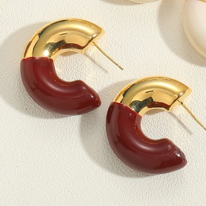Macro shot of C-shaped earrings with gold plating and dark red enamel finish