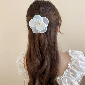 Detailed view of a white lace flower hair clip with yellow pistils on wavy brown hair