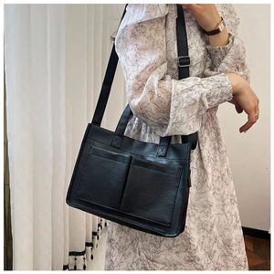 Detail of black faux leather tote bag with large front pockets and adjustable strap