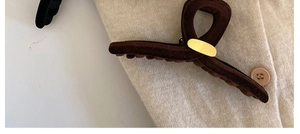 Détail de la pince à cheveux floquée marron foncé avec plaque dorée sur tricot beige