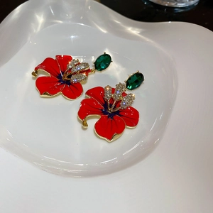 Detail of flower earrings featuring red petals, green gemstones, and sparkling crystals