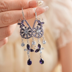 Macro detail of long tassel earrings featuring purple zircon flowers and butterfly charms