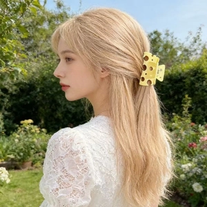 Detail of yellow hollow cheese-shaped hair claw clip worn on blonde hair in a garden