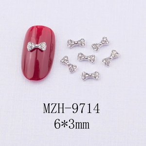 Détail de bijoux d'ongles nœuds argentés 6x3mm avec strass sur manucure rouge