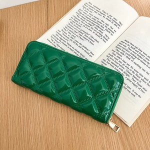 Close-up of a green patent leather wallet with diamond stitching on an open book