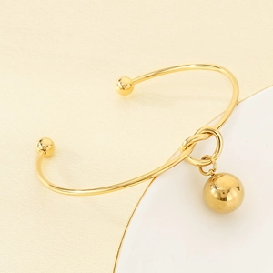 Detail of a golden stainless steel open bangle with bead ends and a hollow sphere pendant