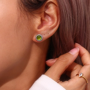 Macro detail of silver-trimmed green gemstone earring and a gold marquise zircon ring