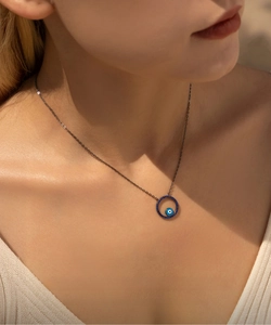 Close-up of a black chain necklace with a blue evil eye pendant on a model's neck