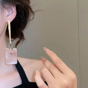 Detail of square marble acetate pendant earrings with gold bar studs on female model